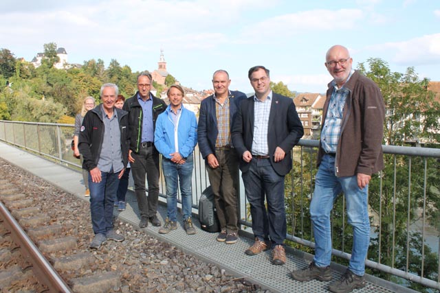 Die beiden Stadtoberhäupter Herbert Weiss (3. von rechts) und Ulrich Krieger (2. von rechts) mit David Baselgia (links aussen) und anderen Baubeteiligten posieren vor dem Teilstück nahe der Codman-Anlage, wo die längste Hängebrücke des Projekts realisiert wird. Foto: Sonja Fasler