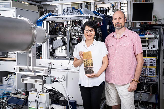 Qing Wu und Benjamin Watts an der cSAXS-Strahllinie, an der sie die Untersuchungen durchführten. Zur Demonstration hält Wu eine Platte mit jeweils einem Segment Blattgold, Zwischgold, Silber (von oben nach unten). Die dunklen Stellen entstehen durch oxidiertes Silber. Foto: Paul Scherrer Institut/Mahir Dzambegovic